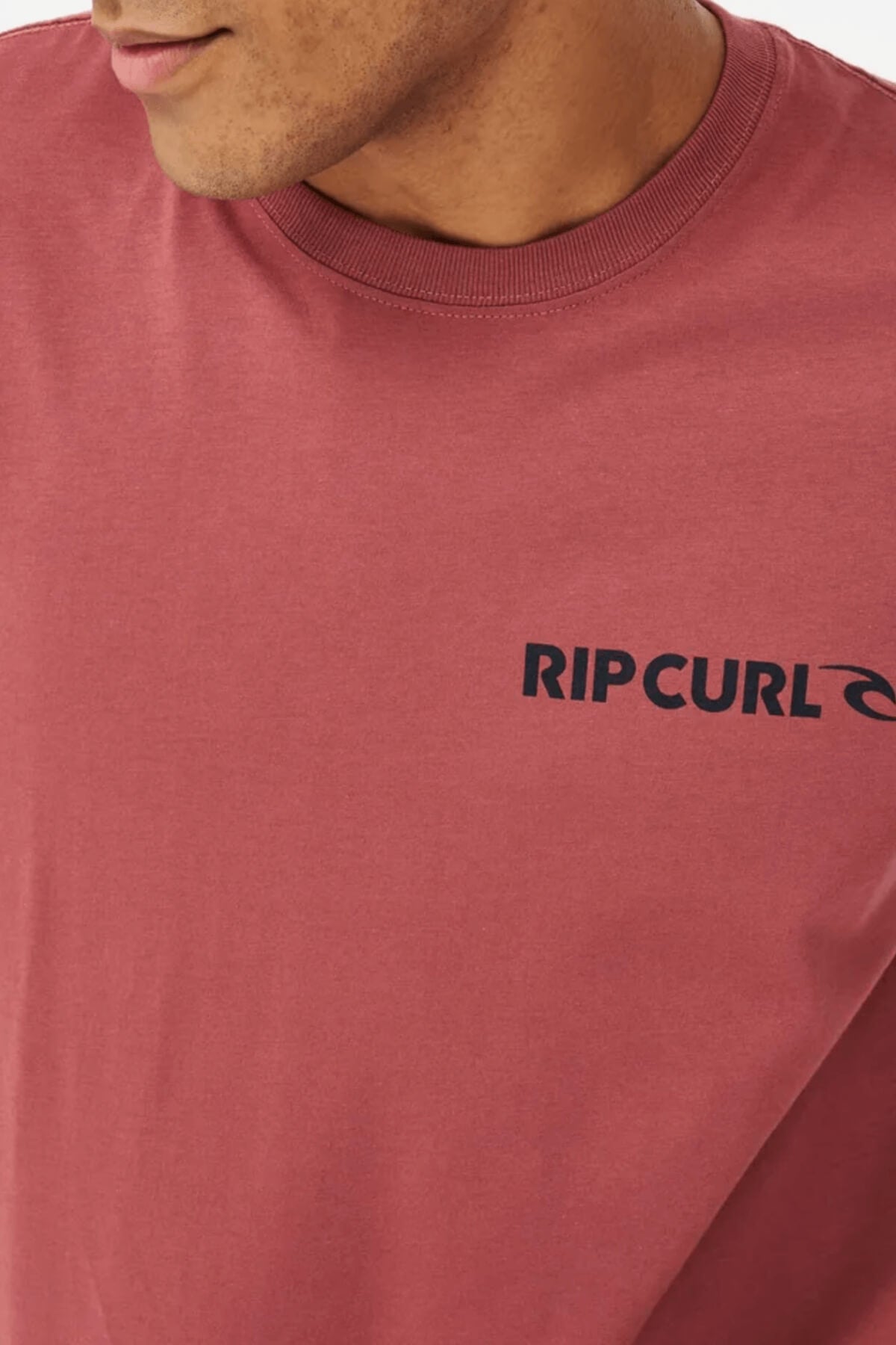 A person in a Rip Curl Brand Icon Tee (100% cotton) with the bold black "RIP CURL" logo on their chest, classic crew neck. The shirt is highlighted, while the person's face is partially visible.