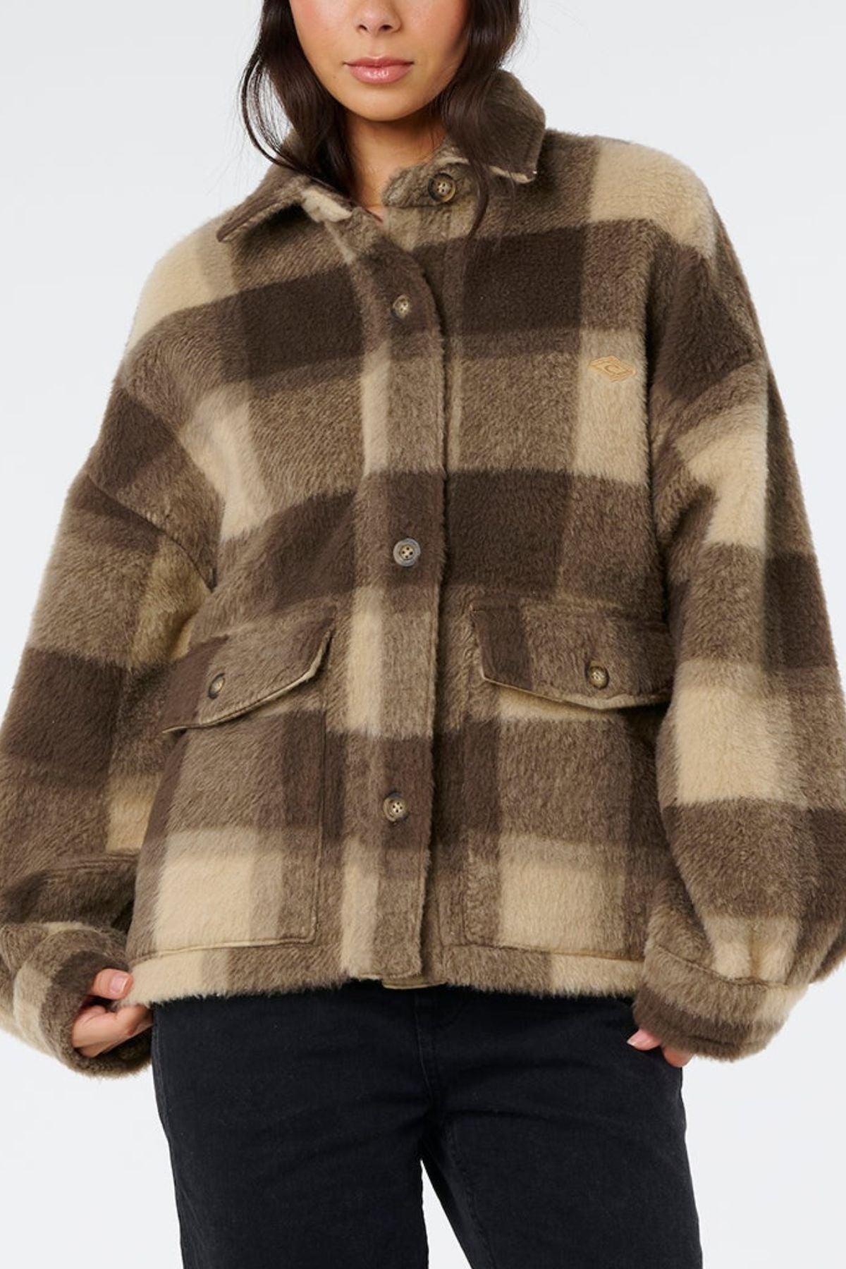 A person wears the Rip Curl Cala Nights Check Jacket—an oversized, beige and brown check design with large buttons and flap pockets—paired with black pants. It features premium construction for a soft, textured look.