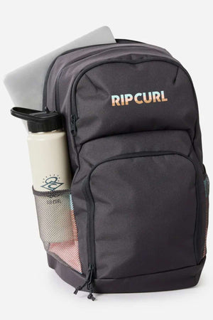 The Rip Curl Chaser 33L Backpack in black, made from recycled polyester, features several zipped compartments, a mesh side pocket with a water bottle, a partially visible laptop in the main section, and the Rip Curl logo on the front.