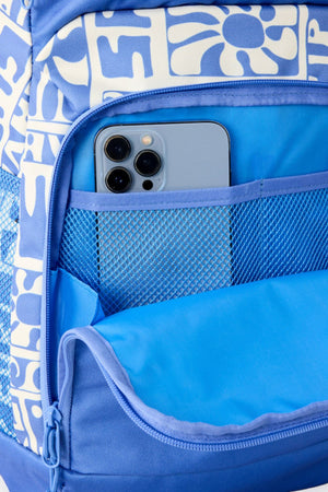 A close-up of a blue patterned Rip Curl Chaser 33L Backpack shows the front pocket unzipped, partially revealing a smartphone with three cameras inside the blue mesh compartment.