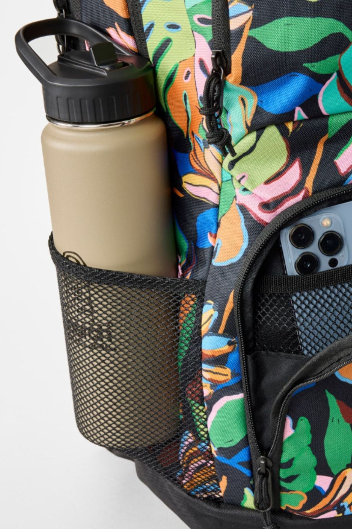 A close-up of the colorful Rip Curl Chaser 33L Backpack made from recycled polyester, with a beige water bottle in the mesh side pocket and a triple-camera smartphone in the front zippered pocket.