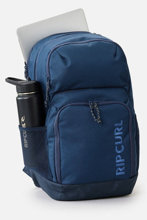 The Rip Curl Chaser 33L Backpack, made from recycled polyester, offers a roomy layout with secure compartments. It comfortably accommodates a 15" laptop in the main section and features a mesh side pocket for your water bottle, making it ideal for people who are constantly on the go!