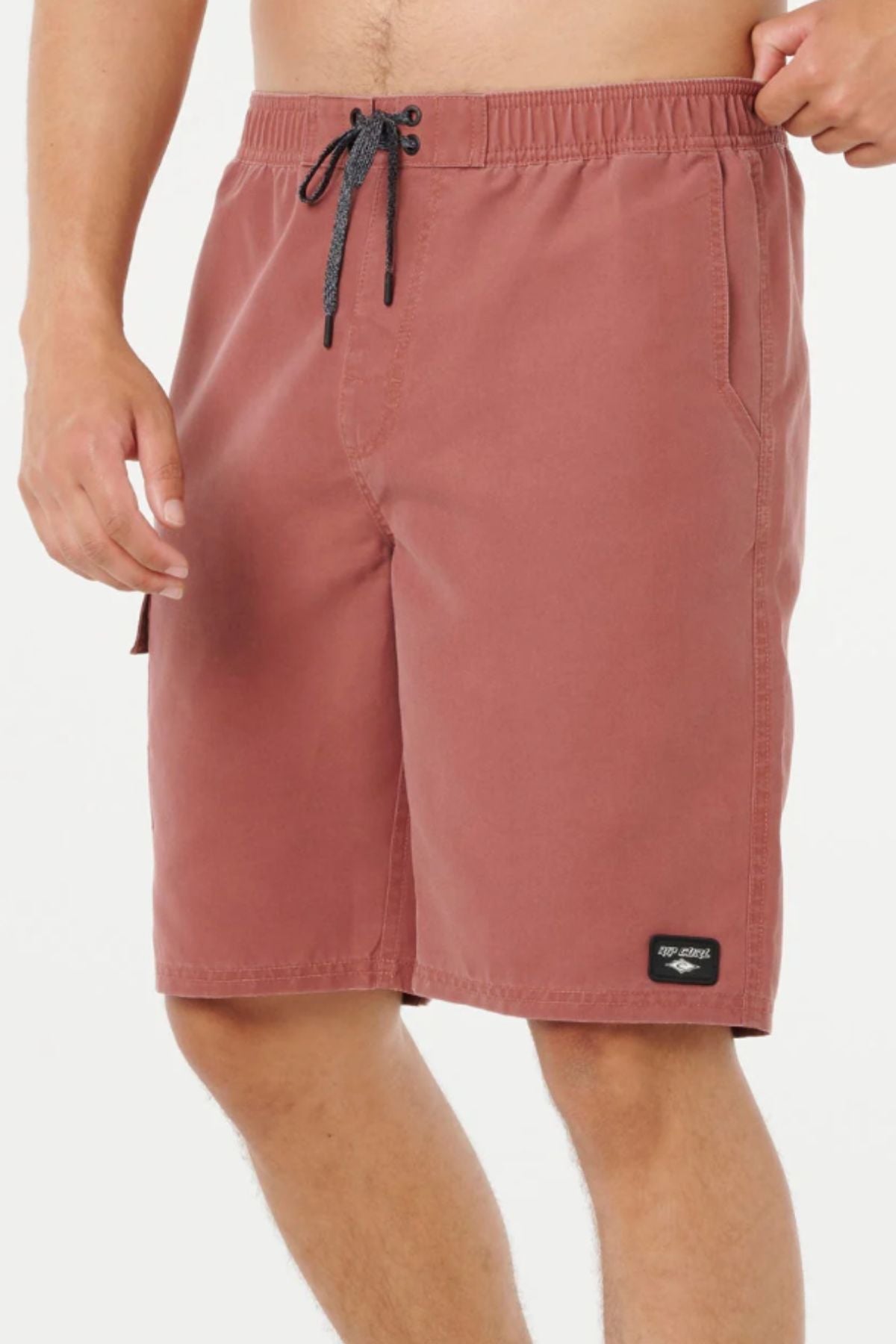 A person wearing Rip Curl Classic Surf Cargo Shorts in dusty rose with a black drawstring and a small black patch near the hem stands against a plain white background.
