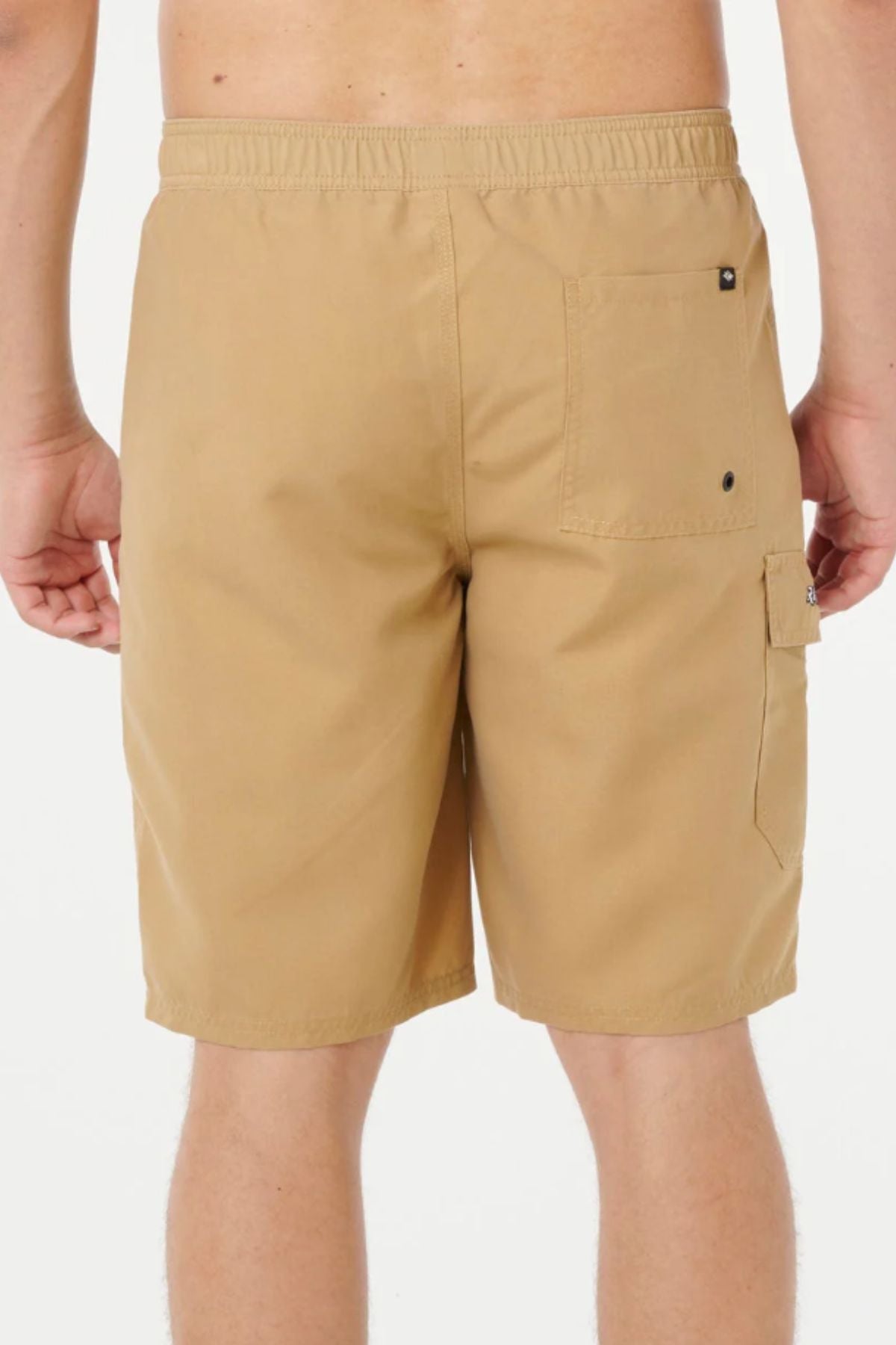 A person is shown from the waist down, wearing tan Rip Curl Classic Surf Cargo Shorts with an elastic waistband, right back pocket, and side flap pocket, standing against a plain white background.