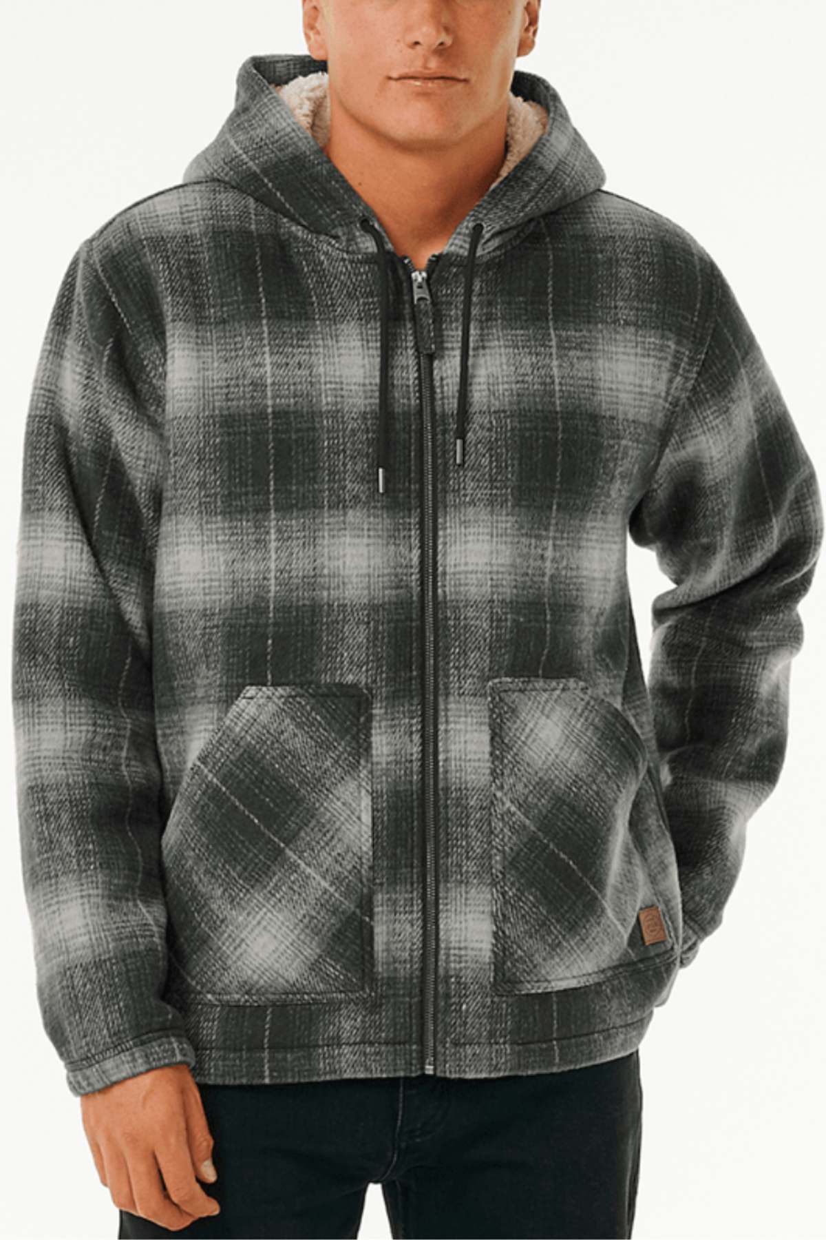Wearing a Rip Curl Classic Surf Check Jacket featuring a black, gray, and white plaid polyester pattern with a sherpa-lined hood and two front pockets, someone stands in dark pants against a plain light background.