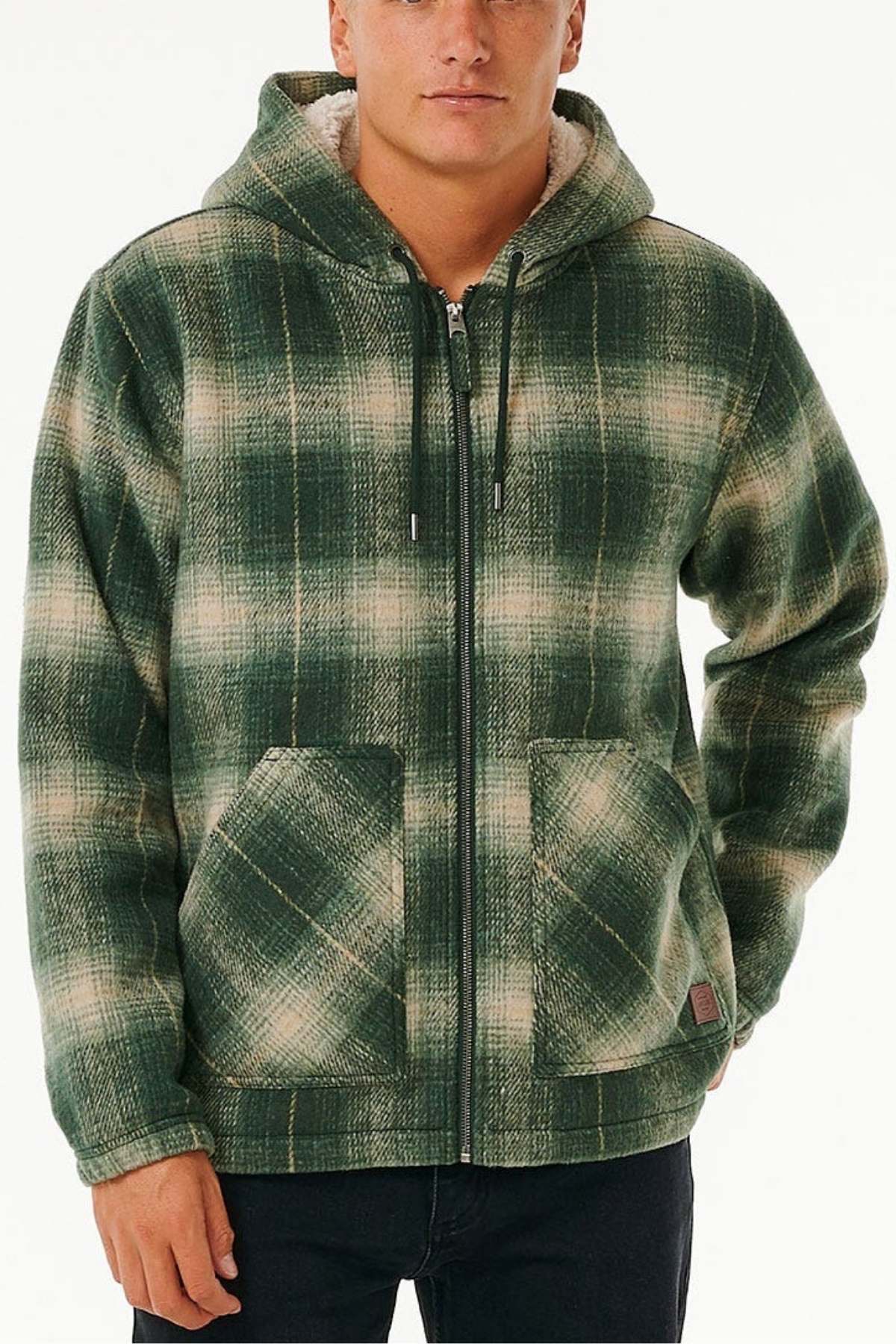 Someone stands against a plain light background wearing the Rip Curl Classic Surf Check Jacket, a green and white polyester plaid zip-up with front pockets and a sherpa-lined hood.
