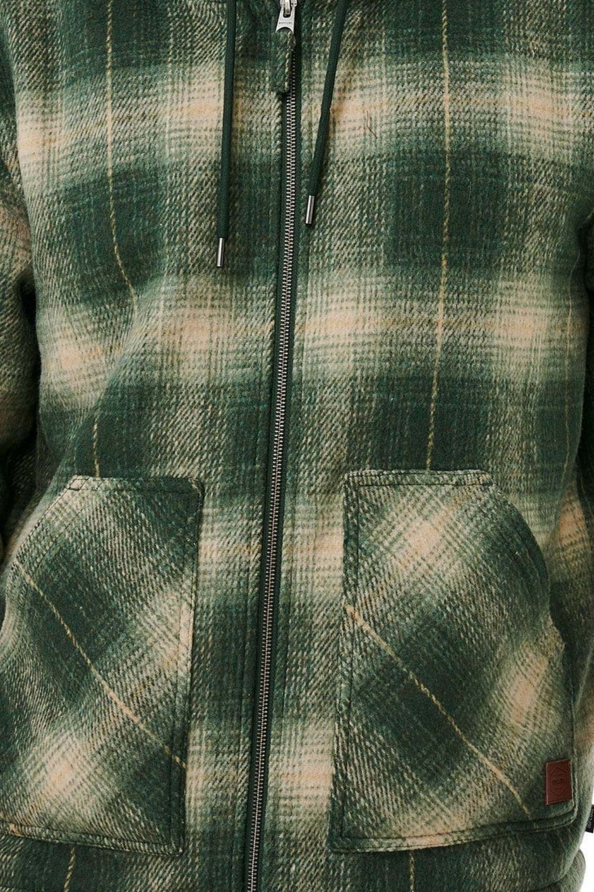 A close-up of the Rip Curl Classic Surf Check Jacket shows its green and beige polyester plaid, zipper front, drawstrings, two spacious pockets, and a cozy sherpa-lined hood for warmth. The fabric has a soft, textured look.