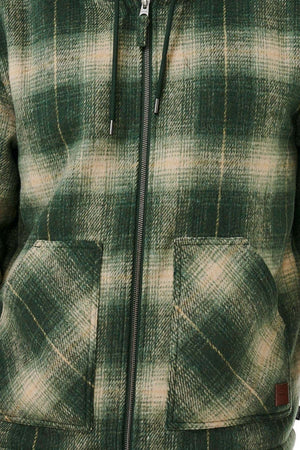A close-up of the Rip Curl Classic Surf Check Jacket shows its green and beige polyester plaid, zipper front, drawstrings, two spacious pockets, and a cozy sherpa-lined hood for warmth. The fabric has a soft, textured look.