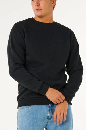 A person wears a Rip Curl Classic Surf Crew black long-sleeve sweatshirt with an embroidered logo and light blue jeans against a white background—an essential surf-inspired addition to any wardrobe.