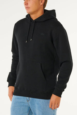 Someone in the Rip Curl Classic Surf Hood in plain black, featuring a front pocket, paired with light blue jeans, stands against a light background.