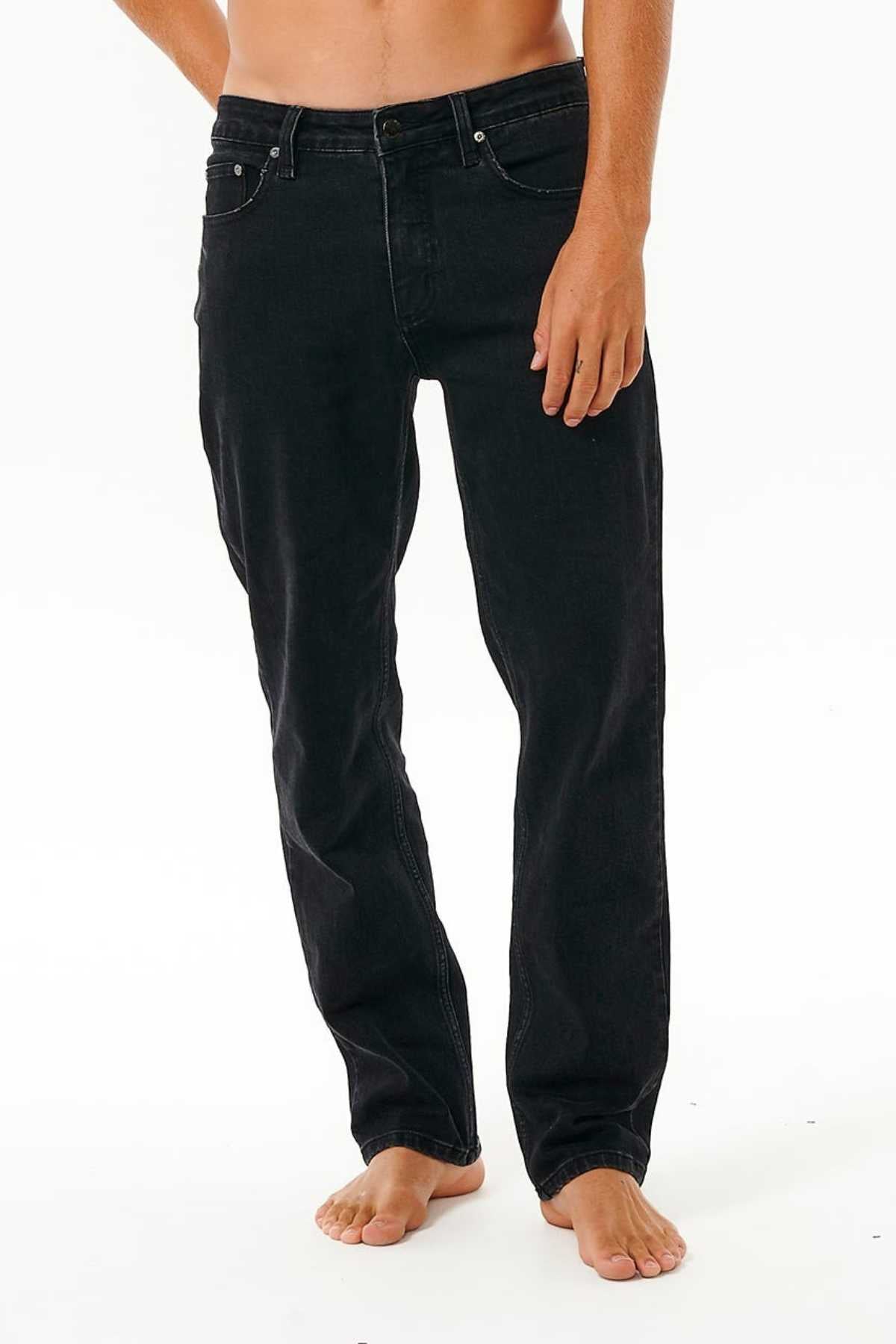 A person stands barefoot in Rip Curl Classic Surf Jeans, made from stretch cotton denim with a five-pocket design and button closure, set against a plain white background. The upper body is partially out of frame.