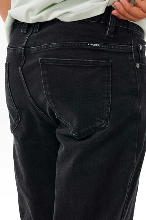 A person wears Rip Curl Classic Surf Jean, crafted from stretch cotton denim, showing visible back pockets and a Rip Curl label above the right pocket, with one hand on their hip.