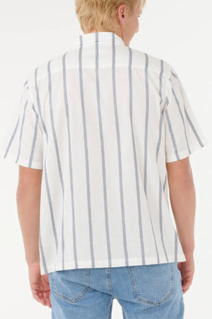 A person with short blond hair is seen from the back, wearing a Rip Curl Classic Surf Stripe Short Sleeve Shirt and light blue jeans, standing against a plain white background.
