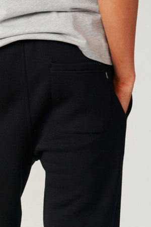 A person wearing a grey shirt and black Rip Curl Classic Surf Trackpant with one hand in their pocket, shown from the waist down—ideal for fans of comfortable casual wear.