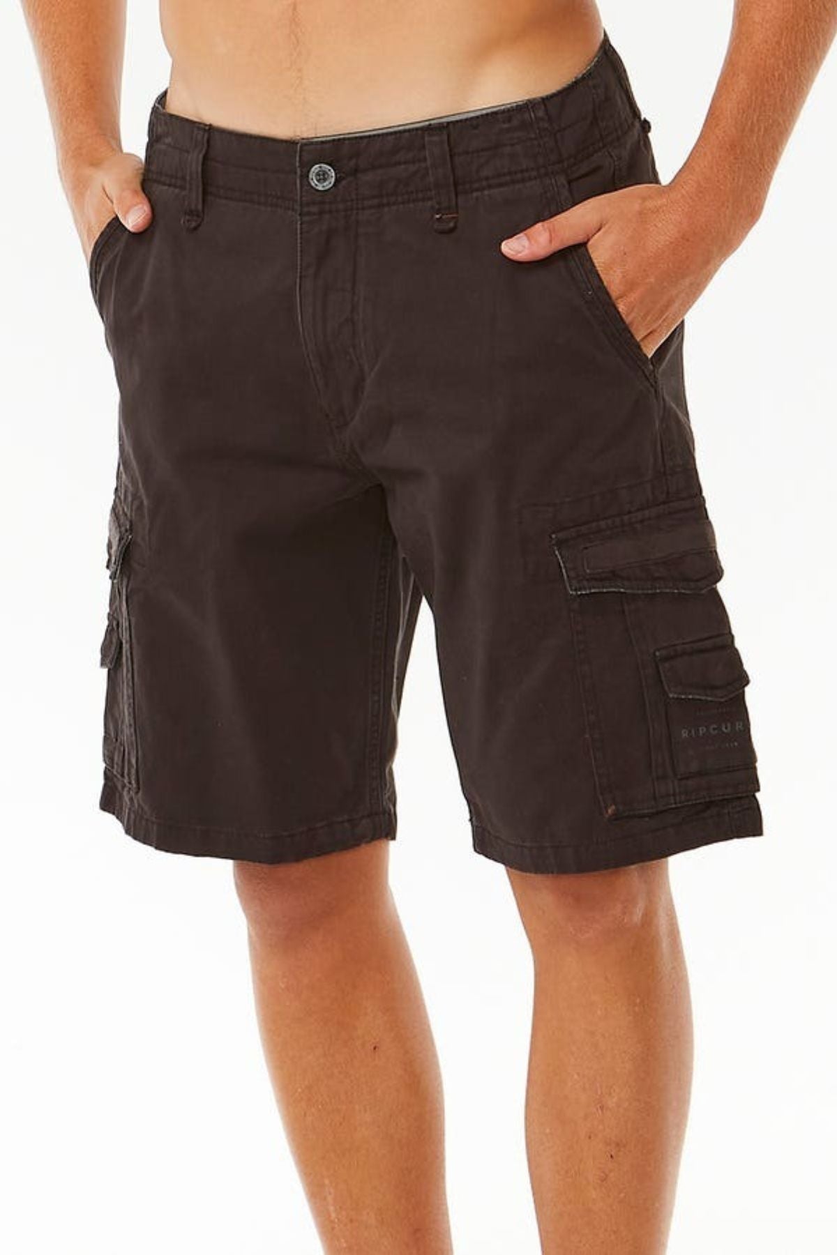 A person is wearing dark brown Rip Curl Classic Surf Trail Cargo Shorts with a relaxed fit, their hands in the pockets. The shorts feature multiple compartments, including two large ones on the sides. The person's head is not visible in the image, which has a plain white background.