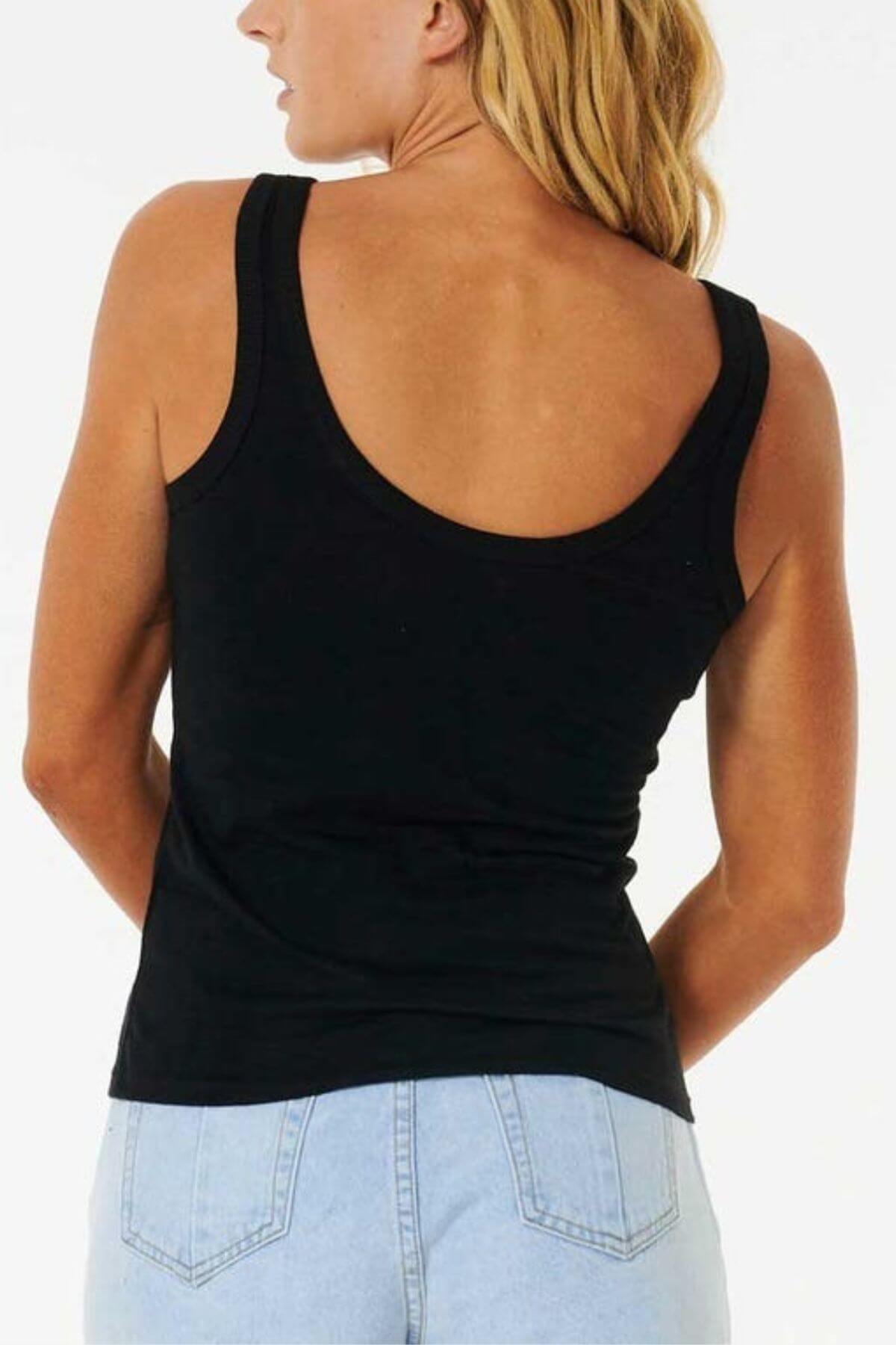 A woman with long blonde hair is shown from the back, wearing a black Rip Curl Classic Tank and light blue jeans against a plain white background.