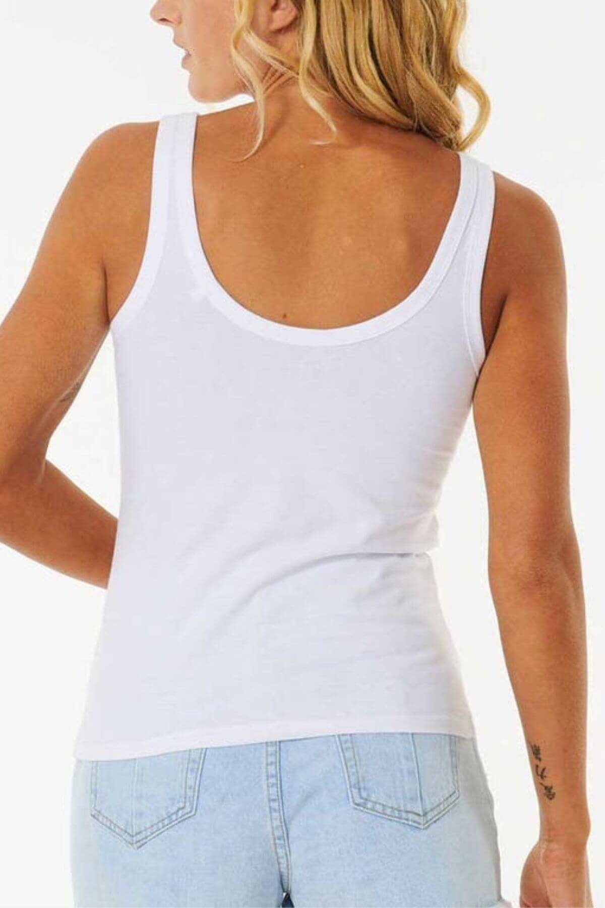 A person with blonde hair, viewed from the back, is wearing a white Rip Curl Classic Tank paired with light blue jeans. The background is plain and white.