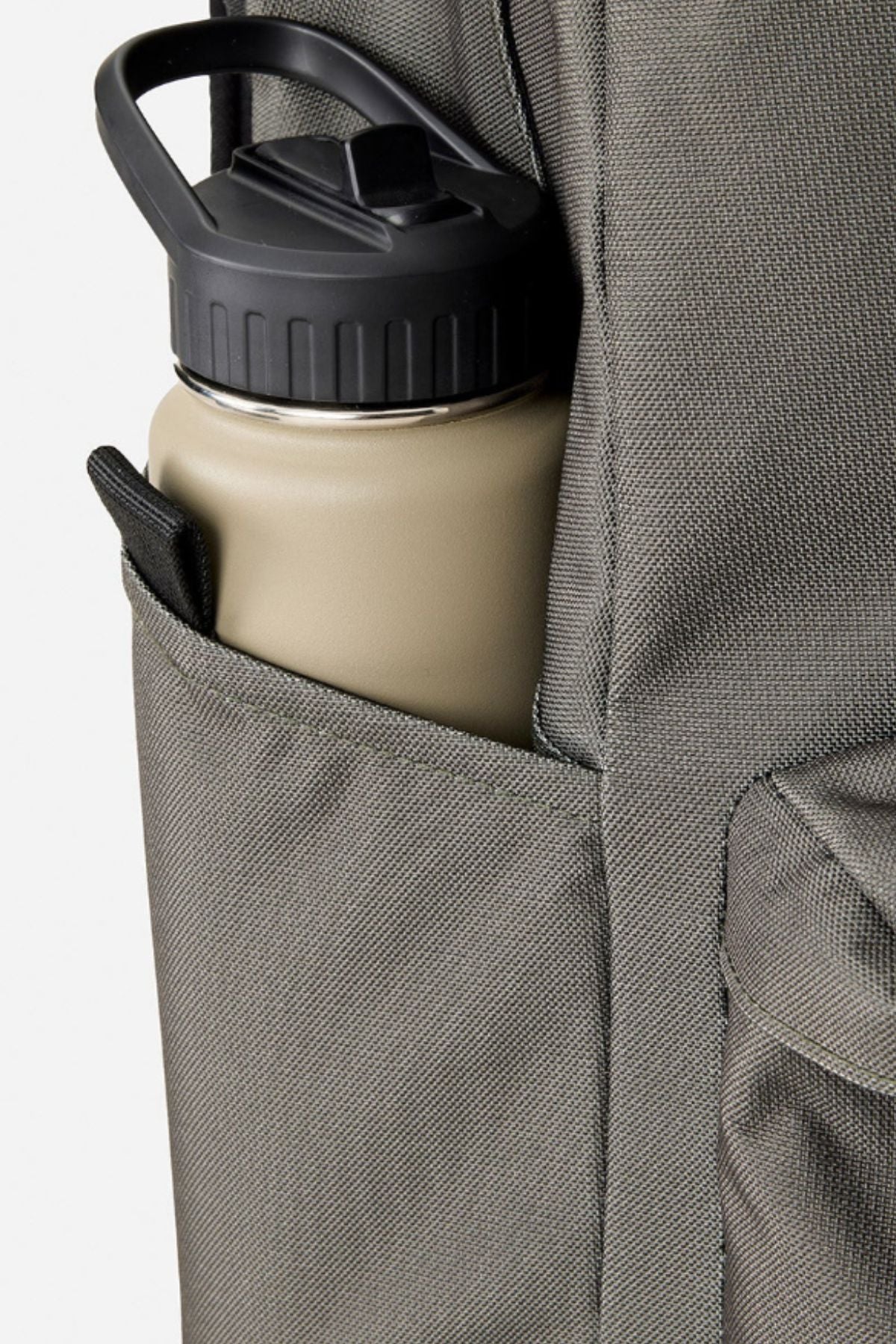 A khaki water bottle with a black lid sits in the side pocket of the gray Rip Curl Crusha 30L Search Backpack, ideal for travel or carrying your laptop.