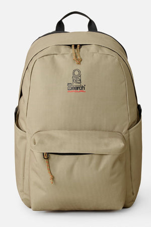 The Rip Curl Crusha 30L Search Backpack is tan with a front zipper pocket, two side pockets, and a black top handle. The front showcases a stylized logo with "Search" in red and black, making it perfect for everyday use.
