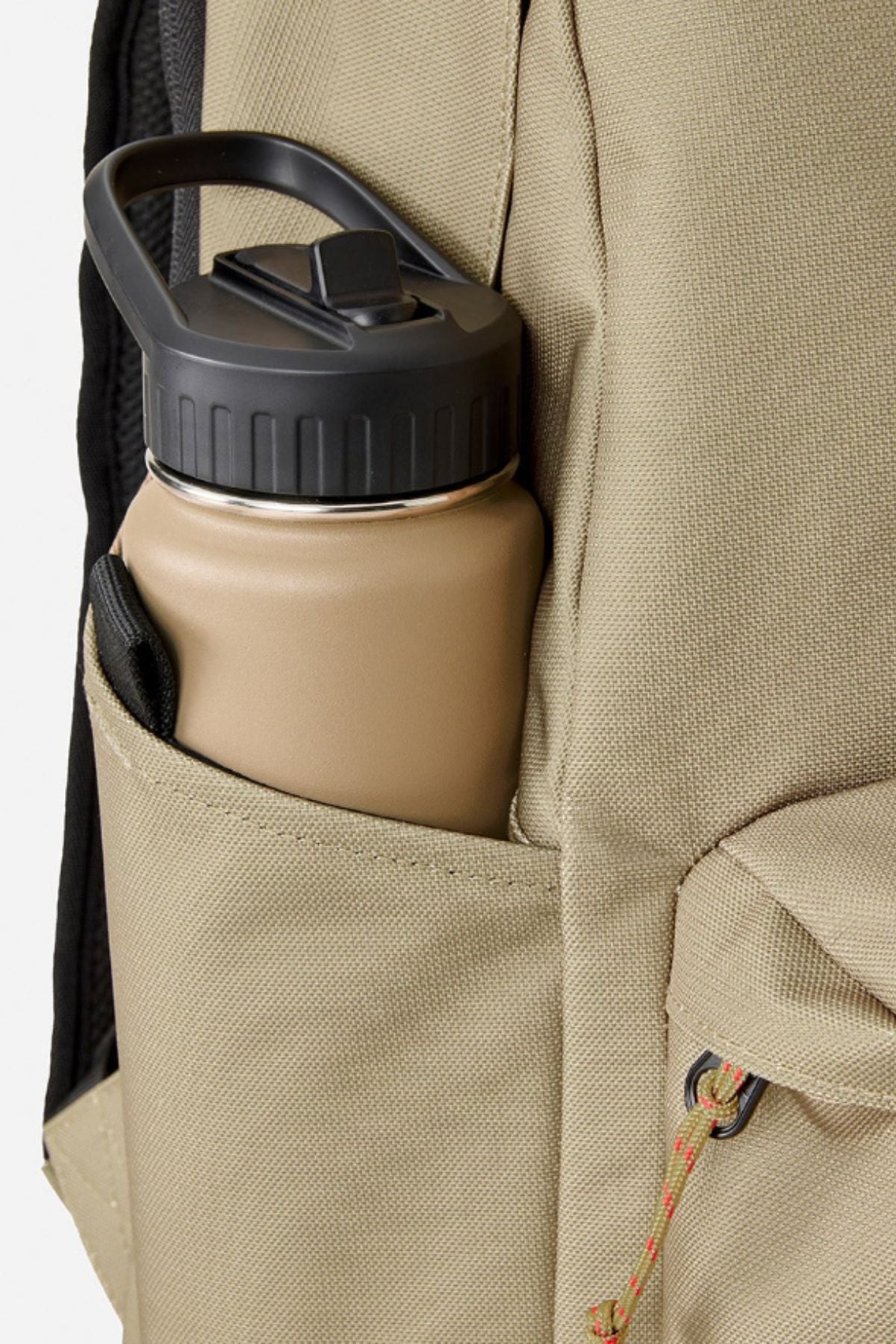 A tan water bottle with a black lid sits in the side pocket of a beige Rip Curl Crusha 30L Search Backpack made from durable fabric.