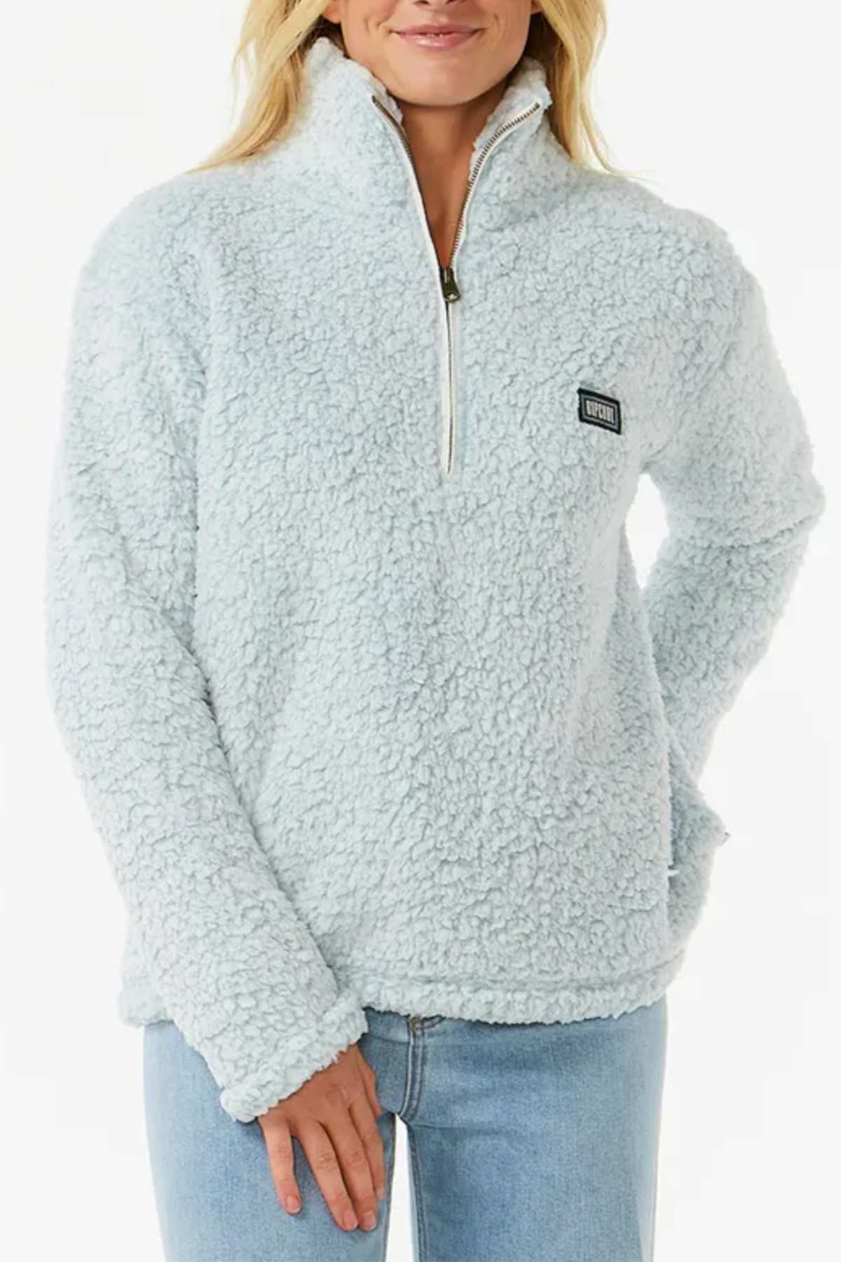 A person is wearing a Rip Curl Dark N Stormy 1/4 Zip Crew, featuring a light blue, fluffy poly marble fleece with a woolly texture and a small rectangular logo patch. They pair it with light blue jeans.