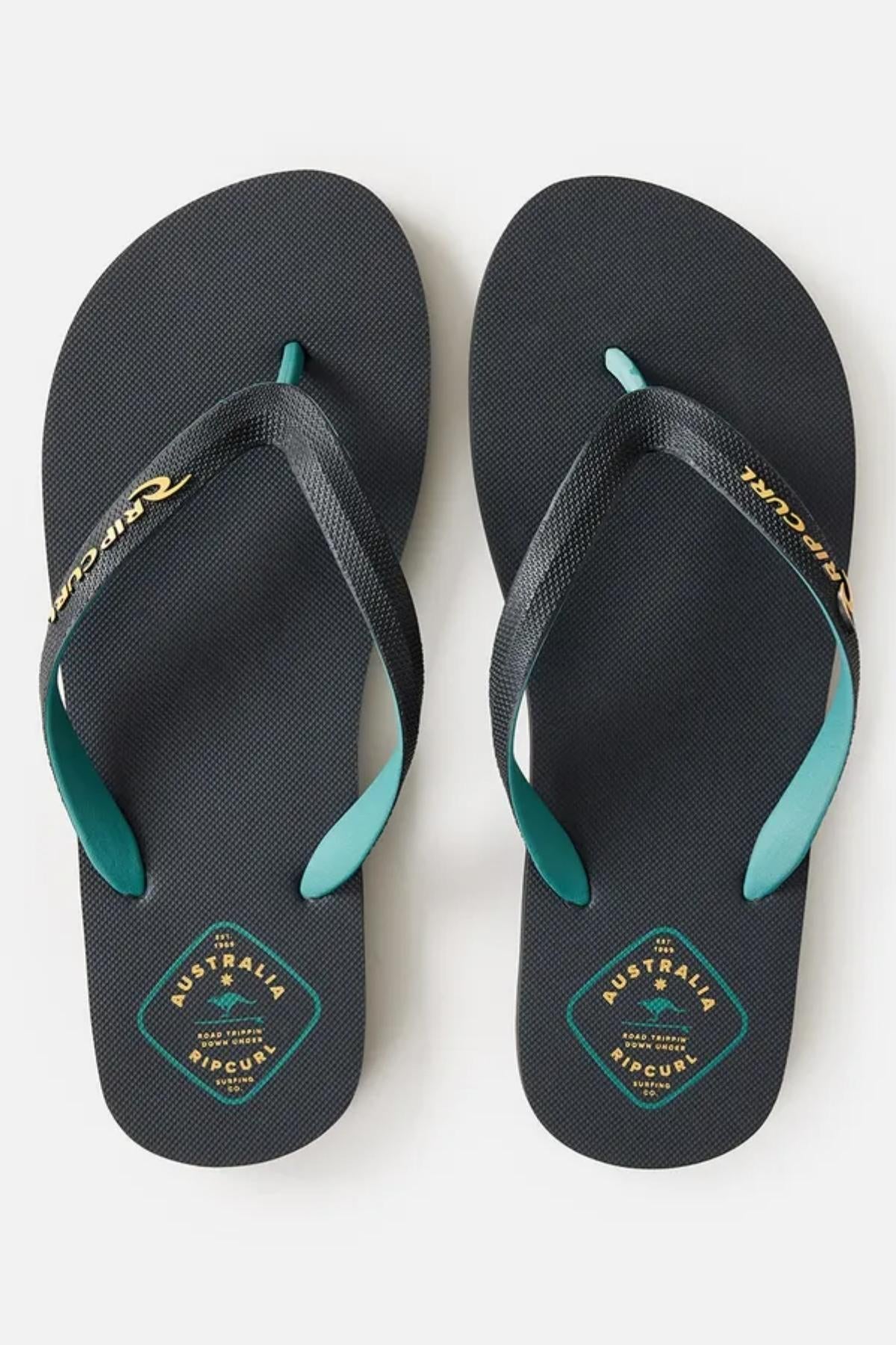 A pair of Rip Curl Desto Bloom Thongs with textured soles. The straps are black with teal accents and feature the brand name in white text. The footbeds have a small logo with the text "Australia" in gold and "Rip Curl" in white, along with a circular design.