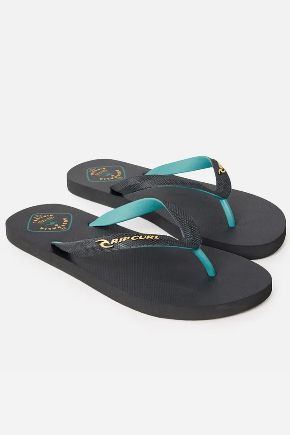 The Rip Curl Desto Bloom Thongs are a pair of black flip-flops with green straps, adorned with the "Rip Curl" logo and a small wave icon in yellow on both the straps and footbed. These flip-flops have a simple, casual design perfect for beachwear.