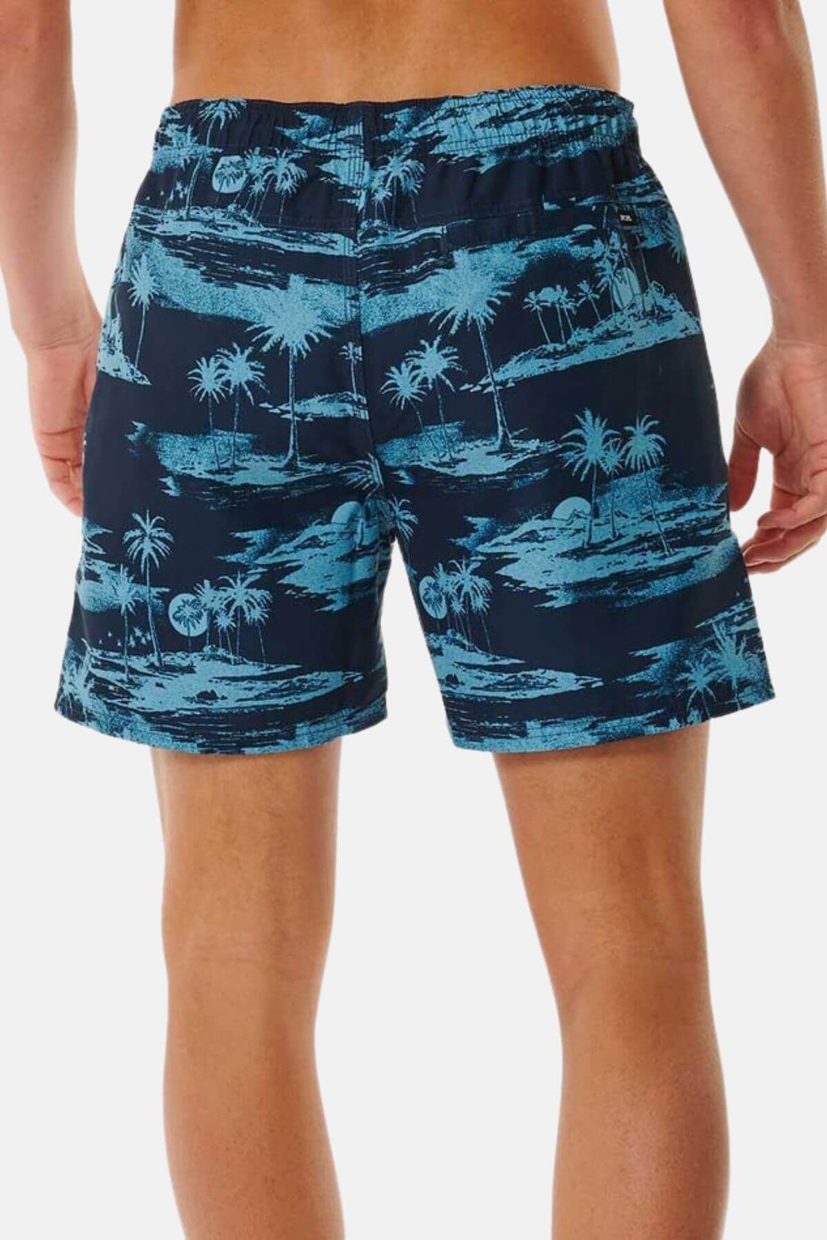 A person is standing with their back to the camera, wearing Rip Curl Dreamers Volley navy board shorts featuring a light blue tropical palm tree print.