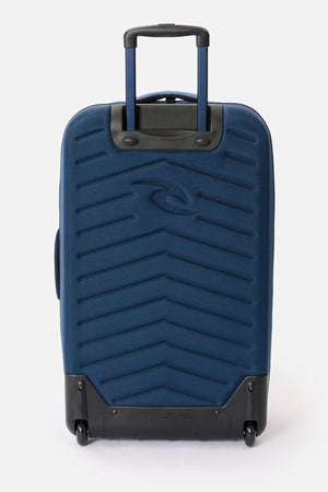 The Rip Curl F-Light Global 100L Cosmic Kiss Wheeled Travel Bag, featuring a blue zigzag pattern, black handle and wheels, and the Rip Curl logo on the front, stands upright against a plain white background.