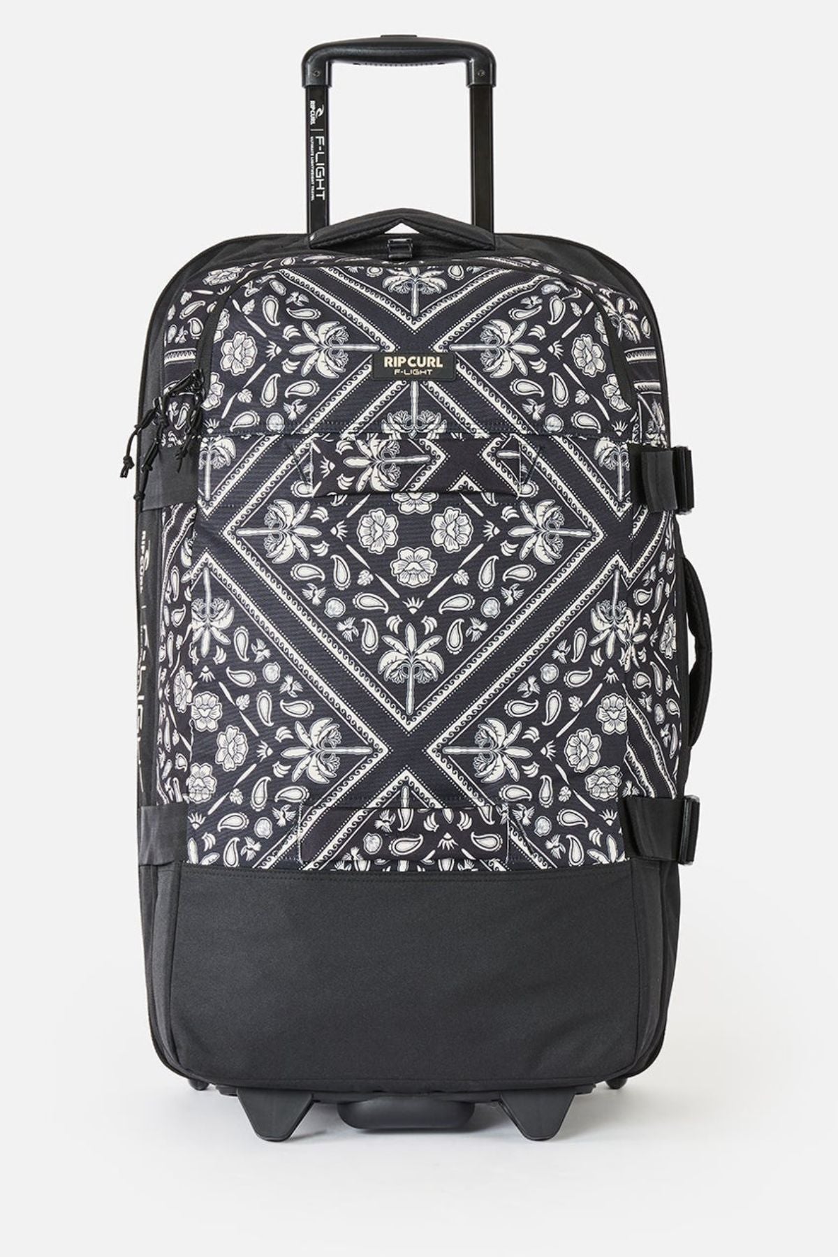 The Rip Curl F-Light Global 100L Bossa Nova is a black check-in roller bag with a white paisley and geometric pattern, telescopic handle, side straps, black bottom, AirTag sleeve, and the Rip Curl logo near the top front.