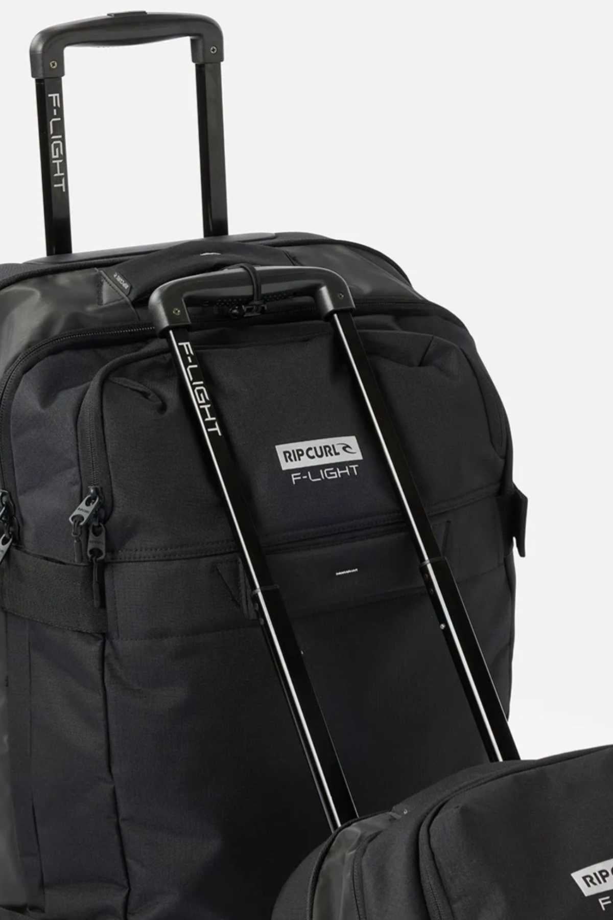 A close-up of two black Rip Curl F-Light Global 100L Icons rolling travel bags with extended handles. The bags prominently display the "F-Light" branding on the handles, and the front pocket of the larger bag features a visible Rip Curl logo. The background is plain white.