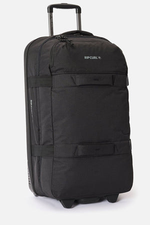 The Rip Curl F-Light Global 100L is a large black check-in roller bag featuring a retractable handle, two front pockets, sturdy side straps, and an AirTag sleeve, shown upright against a plain white background.