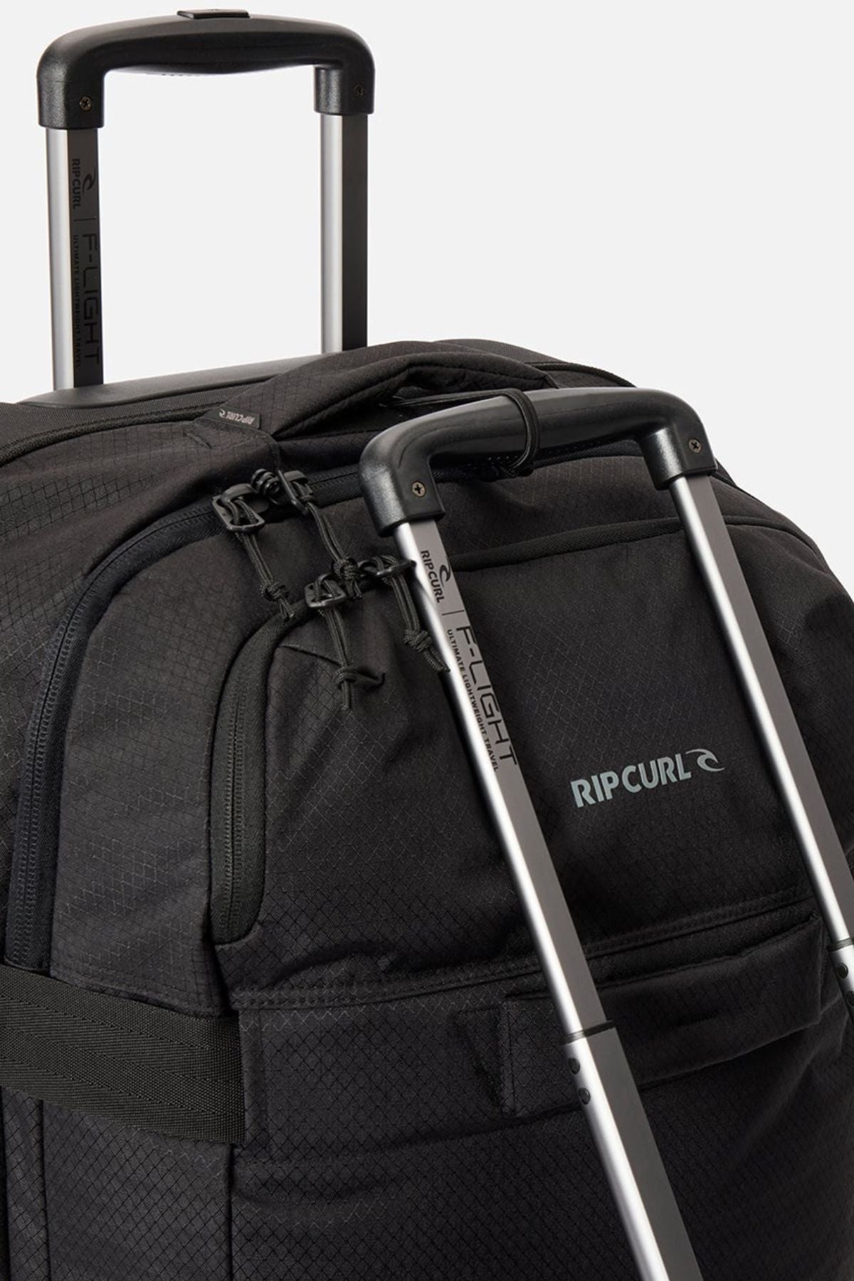 Close-up of two black Rip Curl F-Light Global 100L check-in suitcases with extended silver handles, zippers, and a visible brand logo on the fabric.