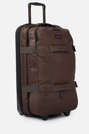 The Rip Curl F-Light Global 100L Search Travel Bag is a brown, wheeled suitcase made from recycled polyester with a black handle stand. It features multiple straps, a front zippered pocket, and a small logo patch near the top. Its compact design makes it ideal for travel.