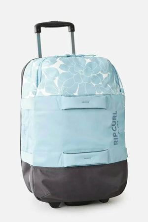 The Rip Curl F-Light Transit 50L Sessions Travel Bag features a light blue and gray design with floral pattern, black wheels and base, retractable handle, side "RIP CURL" branding, and a convenient laptop section.