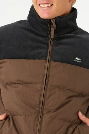 A person smiling, shown from shoulders to mouth, wears the Rip Curl Fade Out Cord Puffer Jacket with a dark corduroy collar, zipper closure, and quilted padding—ideal for outdoor adventure.