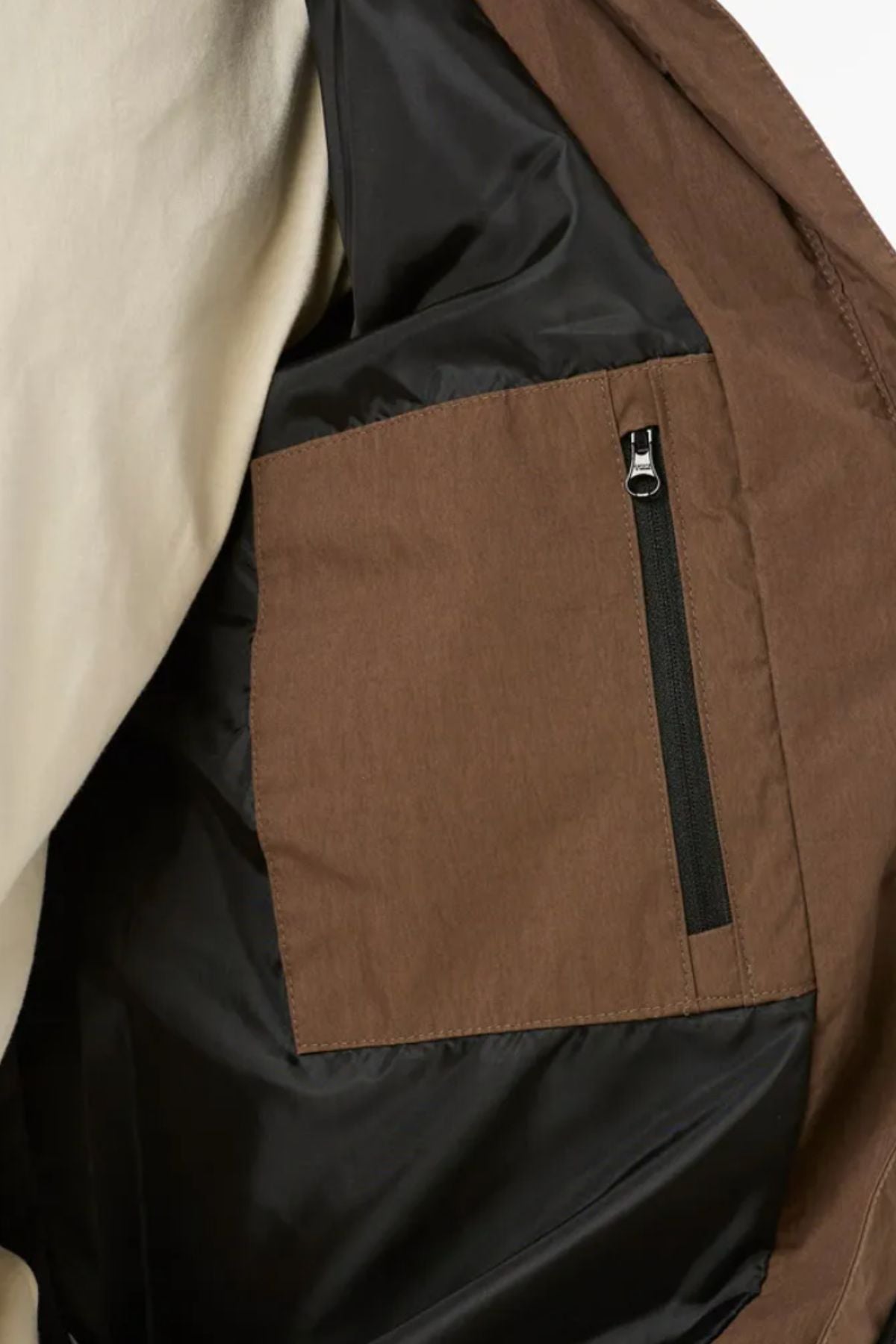 Close-up of the Rip Curl Fade Out Cord Puffer Jacket’s interior, featuring a brown pocket with black zipper on black quilting, plus a glimpse of cream outer fabric—perfect for outdoor adventures.