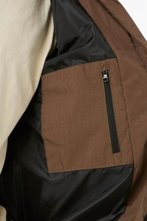 Close-up of the Rip Curl Fade Out Cord Puffer Jacket’s interior, featuring a brown pocket with black zipper on black quilting, plus a glimpse of cream outer fabric—perfect for outdoor adventures.