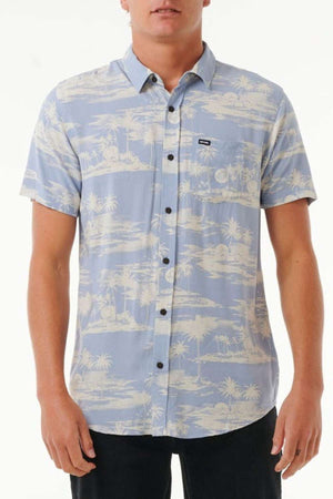 A person wearing a breathable Rip Curl Fun Times Short Sleeve Shirt in light blue, adorned with a tropical palm tree design, stands against a plain background. This shirt includes a button-up front and a convenient chest pocket.