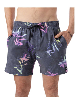 A person wearing the Rip Curl Fun Times Volley, which are dark floral swim shorts with vibrant tropical patterns. These quick-dry shorts have a drawstring waist, and the person has their hands in the pockets against a plain white background.