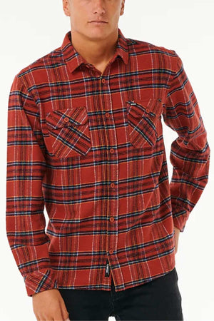 A person donning a Rip Curl Griffin Flannel Shirt in a red and black plaid button-up style, made from cotton flannel with chest flap pockets, stands with one hand on their hip against a plain white background.