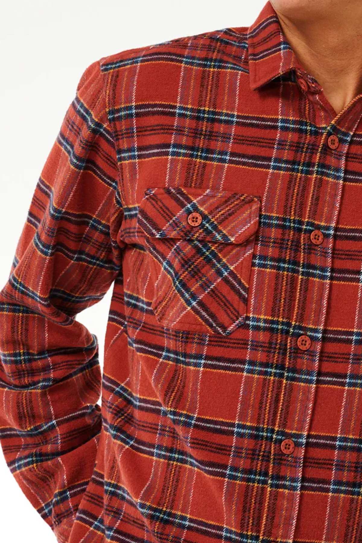 Close-up of an individual wearing the Rip Curl Griffin Flannel Shirt, showcasing its red and black plaid design. The heavy brushed fabric ensures both comfort and warmth. The shirt includes a single chest pocket on the left side with a diagonal plaid pattern and is buttoned up, displaying only the upper torso alongside part of the neck and chin.