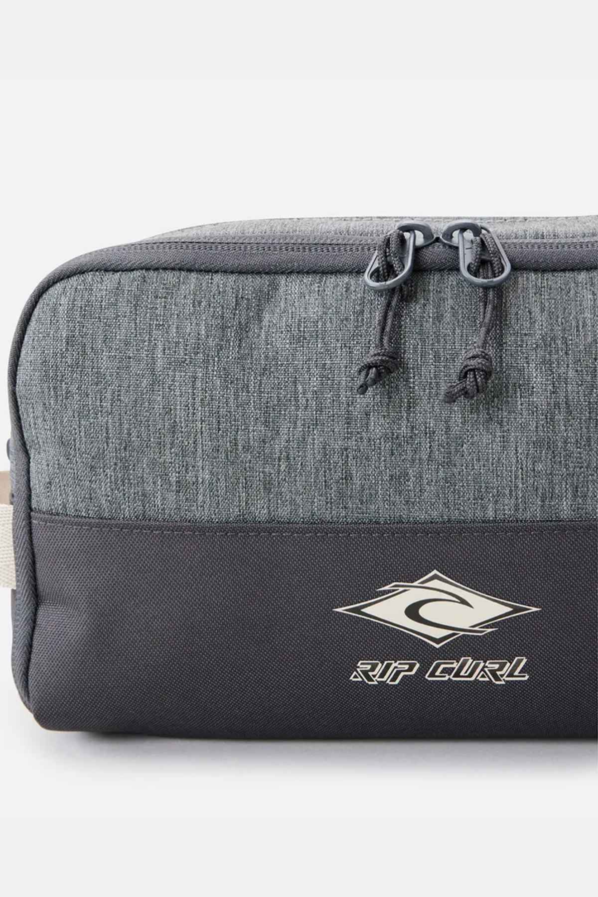 The Rip Curl Groom Classic Surf Toiletry Bag is an eco-friendly gray and black bag featuring a logo with a stylized "R" inside a diamond shape. It boasts a top zippered compartment with two pull tabs, offering a simple yet sporty design.