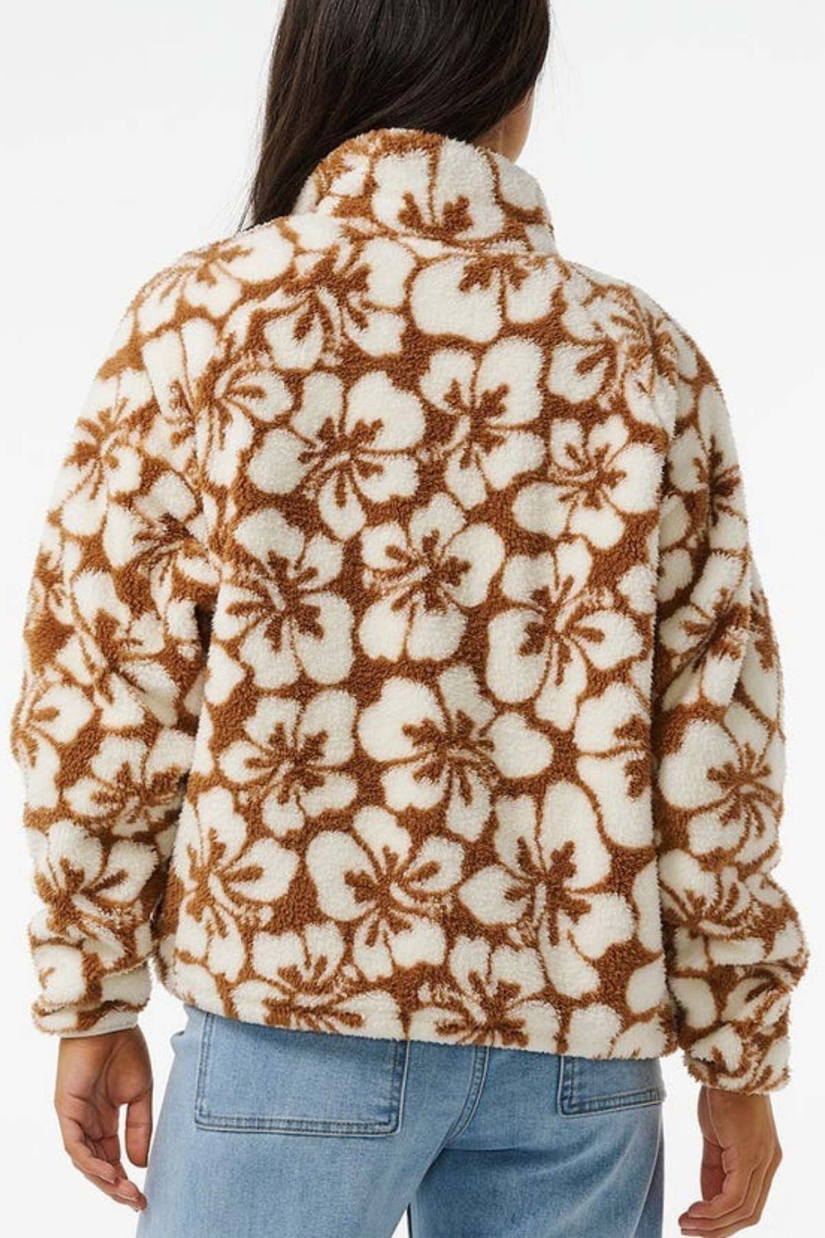 The person in blue jeans, wearing a Rip Curl Hibiscus Heat Polar Fleece Zip Through with a brown and white floral pattern, faces away.