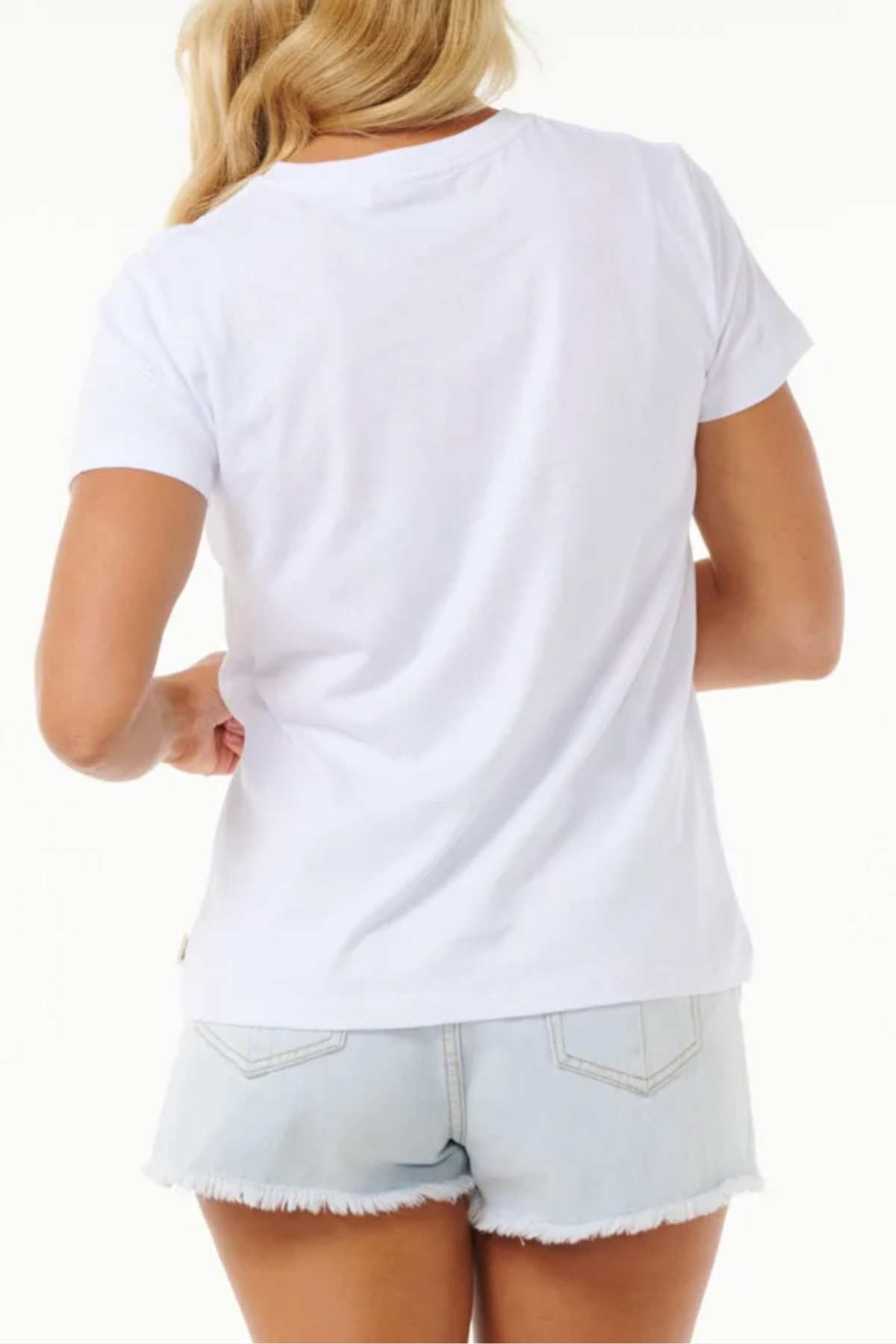 A person with long, blonde hair is facing away from the camera. They are wearing a plain white tee (Rip Curl High Tide Psychic Standard Tee) and Rip Curl High Tide light blue denim shorts with frayed hems. The background is white and unobtrusive.