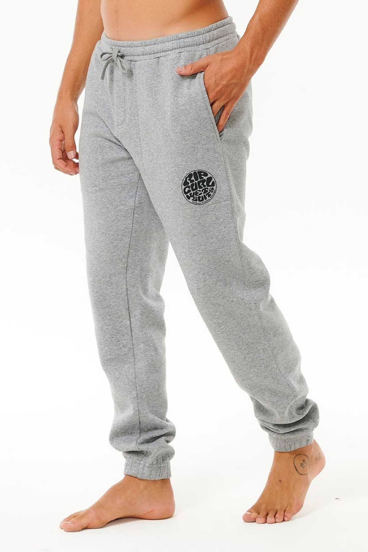 A person stands barefoot on a white background wearing Rip Curl Icons Of Surf Trackpant in light gray organic cotton with a drawstring waist and black circular logo on the left thigh.