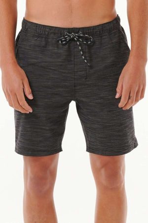 A person wearing the Rip Curl Boardwalk Jackson Volley, featuring charcoal gray quick-dry fabric and an elastic waistband with a black and white drawstring, stands against a plain white background. The boardshort-inspired design showcases a subtle textured pattern on the lower torso and legs.