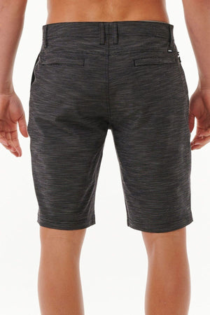 A person is seen from the back wearing Rip Curl Jackson Boardwalk shorts in dark gray with a heather pattern. These quick-dry shorts feature two back pockets and belt loops. The person's hands rest casually at their sides against a plain white background.