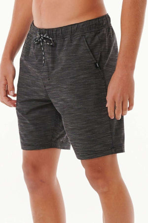 A person wearing Rip Curl Boardwalk Jackson Volley shorts, which are dark gray with a subtle pattern and have an elastic waist, stands against a plain background. These quick-dry shorts, reaching just above the knee, feature side pockets. The person's upper body is not fully visible.