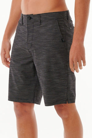 A person stands against a plain background wearing Rip Curl Jackson Boardwalk shorts in knee-length dark gray with a subtle striped pattern. These quick-dry, water-repellent shorts feature pockets on each side and have a button and zip closure. The person is shirtless, with their hands resting naturally by their sides.